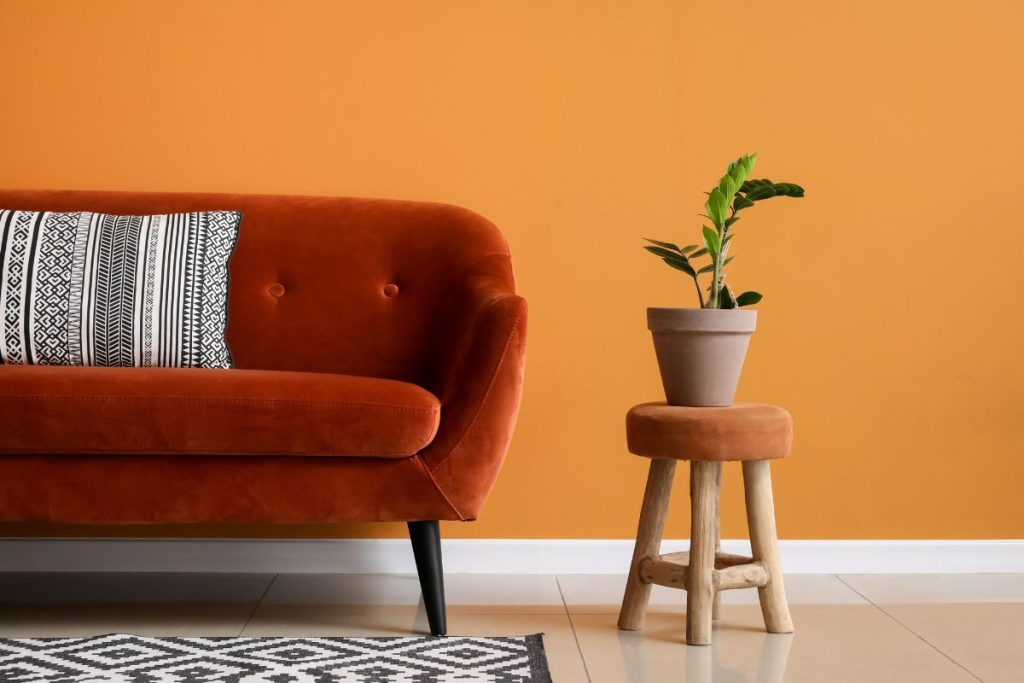 Rostrotes Samtsofa mit Hocker und Zimmerpflanze vor oranger Wand